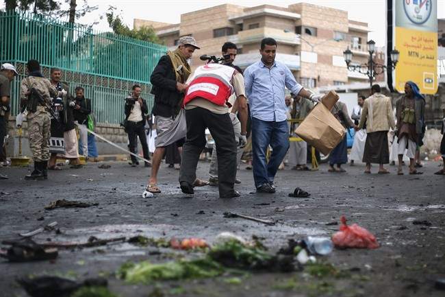 Yemenis security officials with paper bags collect debris as a member of the Yemen Red Crescent Society inspects the site of a suicide bombing in Sanaa, Yemen, Thursday, Oct. 9, 2014. A suicide bomber struck at the center of the Yemeni capital of Sanaa on Thursday, setting off his explosives at a gathering of supporters of the rebel Shiite Houthis who recently overran the city, security officials said.