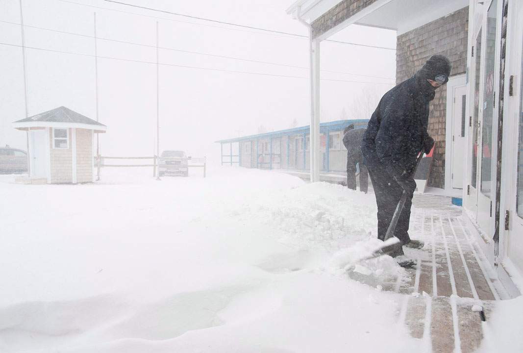 FILE - Alex Mullin shovels snow from the lodge entrance of Poley Mountain ski resort, on Saturday Feb. 9, 2013 in Waterford, N.B.