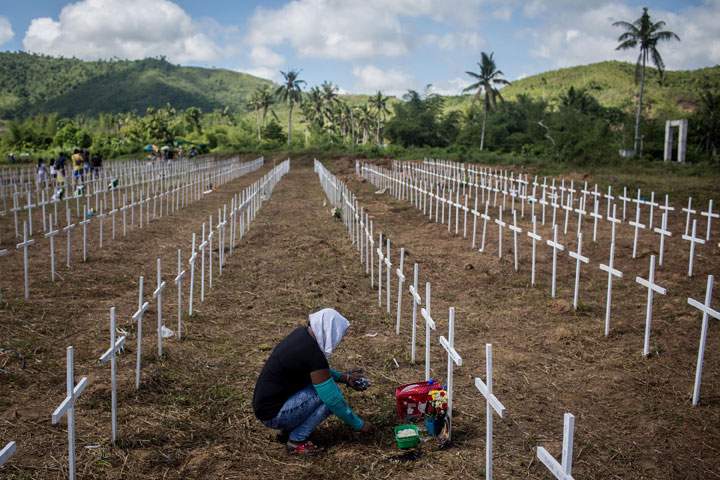A woman sits at the cross of a loved one at the mass grave on the grounds of the Holy Cross Memorial Garden on November 8, 2014 in Tacloban, Leyte, Philippines.
