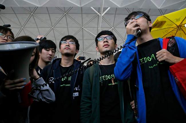 Hong Kong Federation of Students leader Alex Chow, left, committee members Nathan Law, centre, and Eason Chung speak to supporters before attempting to travel to Beijing, at Hong Kong International Airport Saturday, Nov. 15, 2014.