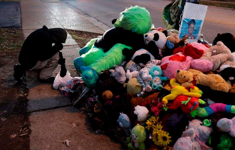 A protester kneels next to a memorial in the middle of the street, Monday, Nov. 24, 2014, more than three months after a black 18-year-old man was shot and killed there by a white policeman in Ferguson, Mo. 