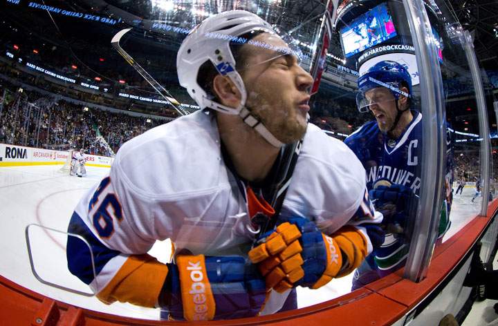 New York Islanders’ Matt Donovan, left, is checked into the glass by Vancouver Canucks’ Henrik Sedin during first period NHL hockey action in Vancouver, B.C., on Monday March 10, 2014.