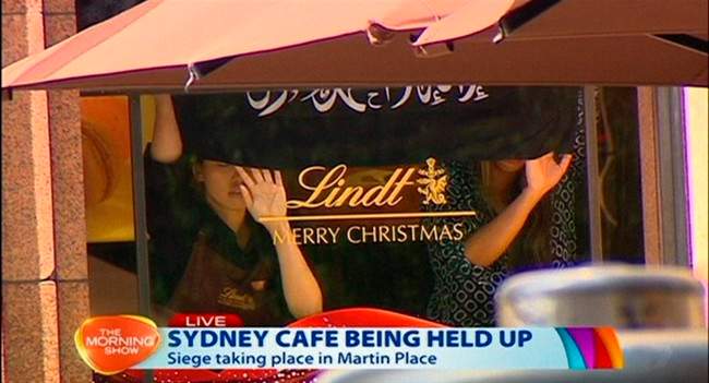 This image taken from video shows people holding up what appeared to be a black flag with white Arabic writing on it, inside a cafe in Sydney, Australia Monday, Dec. 15, 2014. An apparent hostage situation was unfolding inside the chocolate shop and cafe in Australia’s largest city on Monday, where several people could be seen through a window with their hands held in the air.