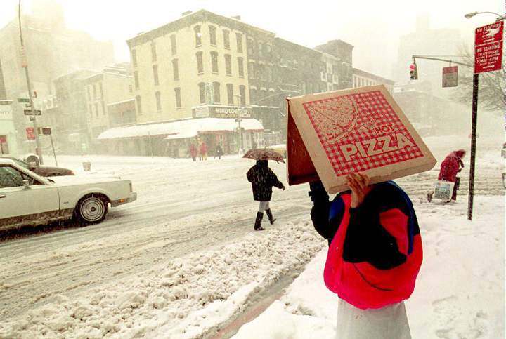A pizza delivery man shields himself from the blizzard conditions pounding New York City and most of the east coast of the U.S. as he waits to cross second Avenue 13 March 1993.