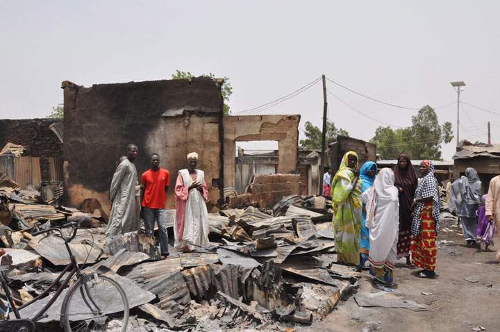 In this Sunday, May 11, 2014 file photo, people stand outside burnt houses following an attack by Islamic militants in Gambaru, Nigeria. Cameroon's government said Tuesday that its military killed 143 militants from the Islamic extremist group Boko Haram, which has been waging war in neighbouring Nigeria. 