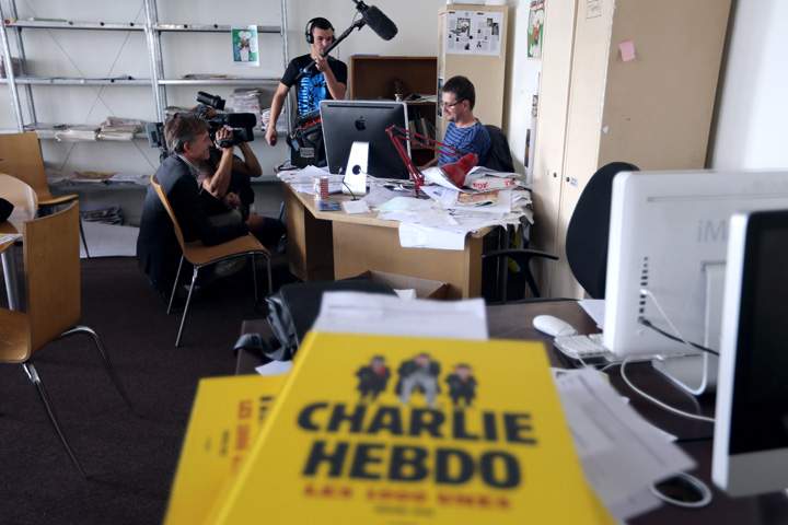 French satirical weekly Charlie Hebdo’s publisher and cartoonist, known as Charb (R), works at his desk on an issue which features a satirical drawing he drew, entitled ‘Intouchables 2’, while journalists are filming an recording, on September 19, 2012 at the weekly’s headquarters in Paris.