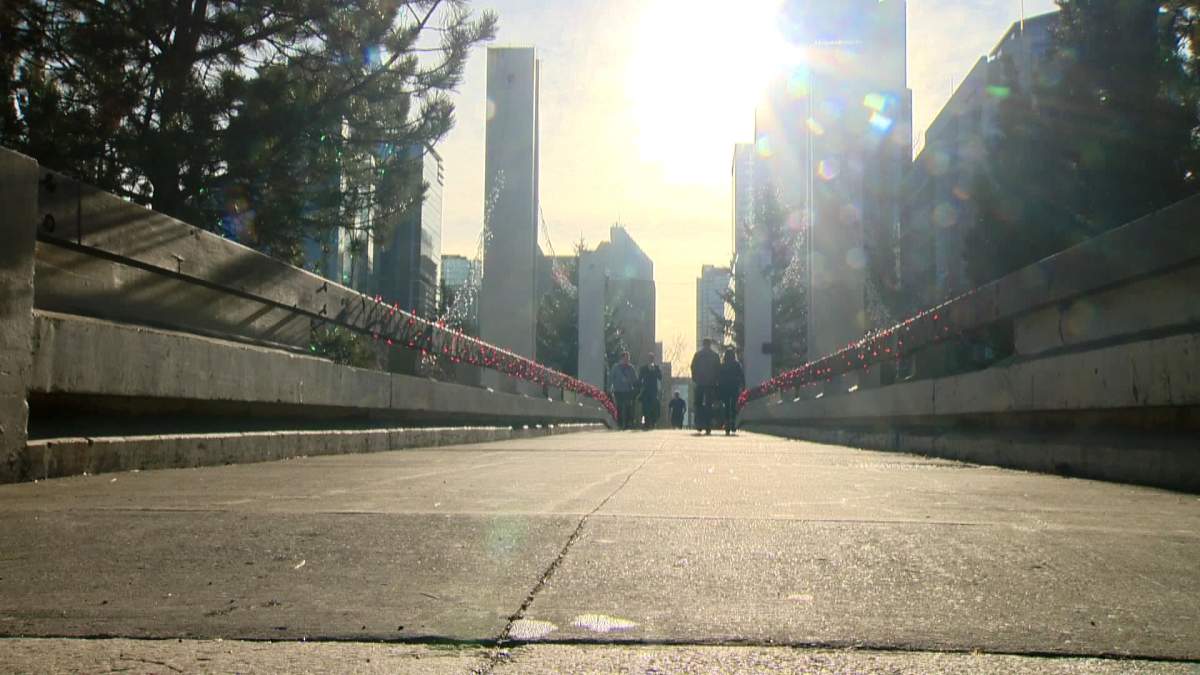 People stroll along a pedestrian bridge on a sunny day in Calgary.