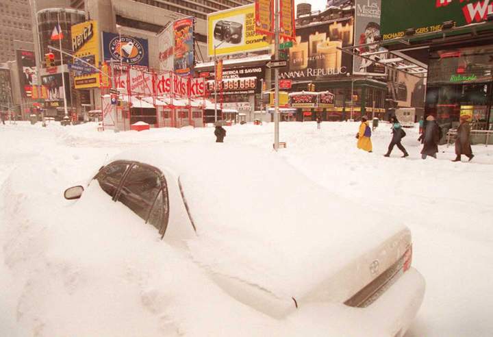 Pedestrians make their way past a buried car in New York’s Times Square after the city was hit by one of the worst snow storms in recent history on Jan. 8, 1996..