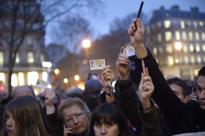 Journalists raise their press cards as others hold up pens during a gathering at the Place de la Republique (Republic square) in Paris, on January 7, 2015.