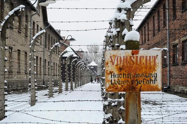 Visitors walk between barbed wire fences at the Auschwitz Nazi death camp in Oswiecim, Poland, Monday, Jan. 26, 2015. Poland's president has signed legislation that outlaws blaming Poland as a nation for Holocaust crimes committed by Nazi Germany.