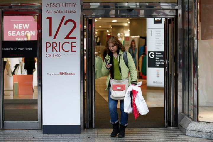 A shopper checks her mobile device as she exits a BHS department store, operated by Arcadia Group Ltd., in London, U.K., on Monday, Jan. 26, 2015.