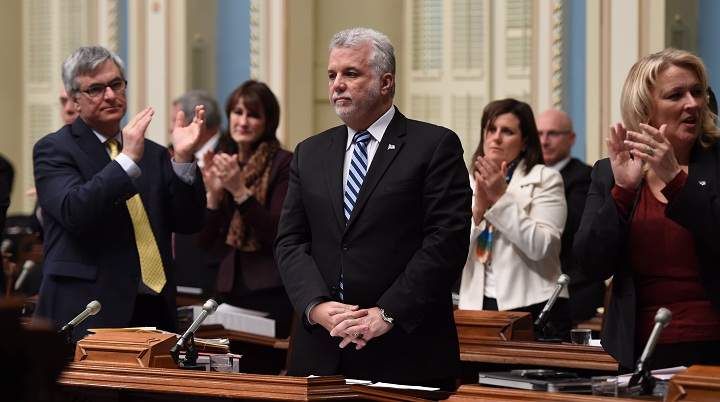 Quebec Premier Philippe Couillard, centre, stands as all members of the legislature applaud after he praised the work of former Education Minister Yves Bolduc, Thursday, February 26, 2015 at the legislature in Quebec City. Bolduc announced his resignation earlier in the morning. Government legislature leader Jean Marc Fournier, left, and Quebec Public Security Minister Lise Theriault, right, applaud.