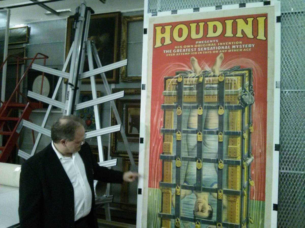 Christian Vachon stands in front of a poster promoting Houdini’s famous upside-down water torture escape.