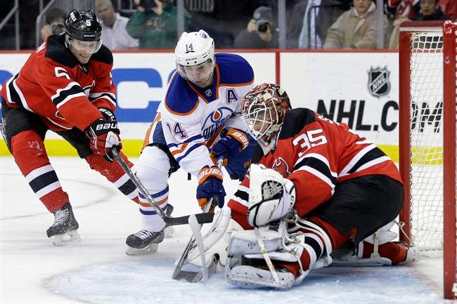 Edmonton Oilers right wing Jordan Eberle (14) tries to get the puck past New Jersey Devils defenseman Adam Larsson (5), of Sweden, and goalie Cory Schneider (35) during the first period of an NHL hockey game Monday, Feb. 9, 2015, in Newark, N.J. (AP Photo/Mel Evans).