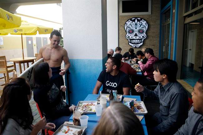 In this Feb. 20, 2015 photo, Nathan Seymour, top left, with a surfboard, chats with his friends at U.S. Taco Co., which is owned by Taco Bell, in Huntington Beach, Calif. As people increasingly reach for foods that stray from the norm and seem less processed, some companies are testing whether it would pay to tuck away their famous logos in favor of more hipster guises. (AP Photo/Jae C. Hong).