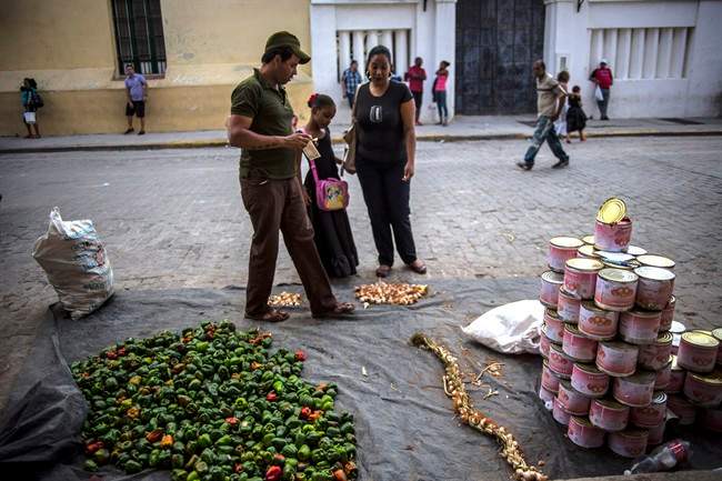 A vegetable street vendor who sells bell peppers, garlic and cans of crushed tomatoes, attends to a woman and her daughter in Old Havana, Cuba, Tuesday, Feb. 17, 2015.