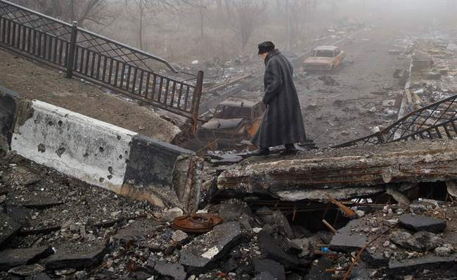 An elderly woman walks across a destroyed bridge, near the scene of heavy fighting in Donetsk, Ukraine, Sunday, March 1, 2015. 