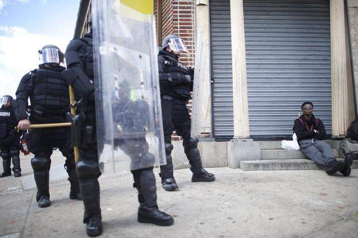 Kyle Mayden, 15, sits on steps of a closed store beside a phlanx of Baltimore policemen in riot gear across the street from the burned CVS pharmacy the afternoon after citywide riots on April 28, 2015 in Baltimore, Maryland.