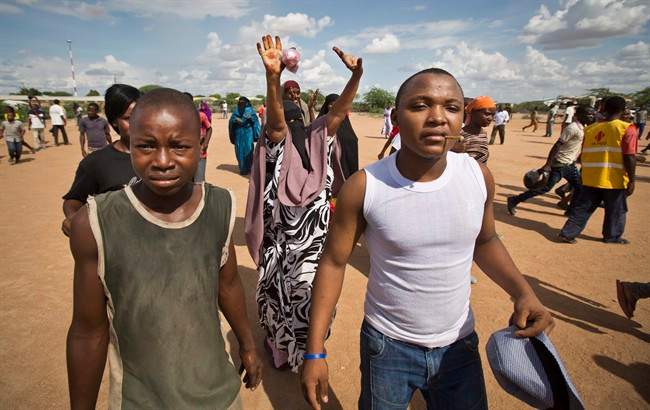 A woman, centre, raises her hands in the air as she and other members of the public get a glimpse, as authorities display the bodies of the alleged attackers before about 2,000 people in a large open area in central Garissa, Kenya Saturday, April 4, 2015.