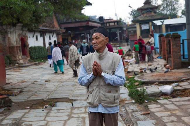 A Nepalese elderly man prays next to a building damaged in Saturday's earthquake, not pictured, in Kathmandu, Nepal, Monday, April 27, 2015.