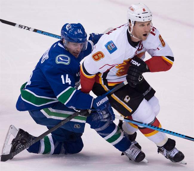 Vancouver Canucks left wing Alex Burrows (14) fights for control of the puck with Calgary Flames defenseman Dennis Wideman (6) during the second period of NHL playoff action in Vancouver, B.C. Wednesday, April 15, 2015. Burrows was taken to hospital Tuesday after suffering an unspecified injury at the team's morning skate.THE CANADIAN PRESS/Jonathan Hayward.