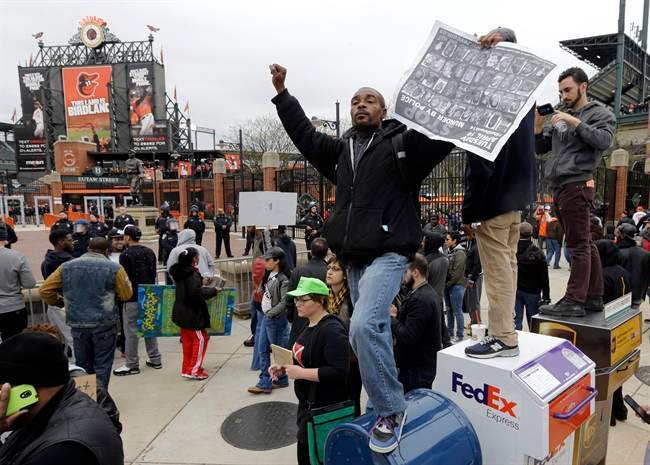 A protestor stands on a mailbox outside of Oriole Park at Camden Yards before a baseball game between the Boston Red Sox and the Baltimore Orioles after a rally for Freddie Gray, Saturday, April 25, 2015, in Baltimore. 