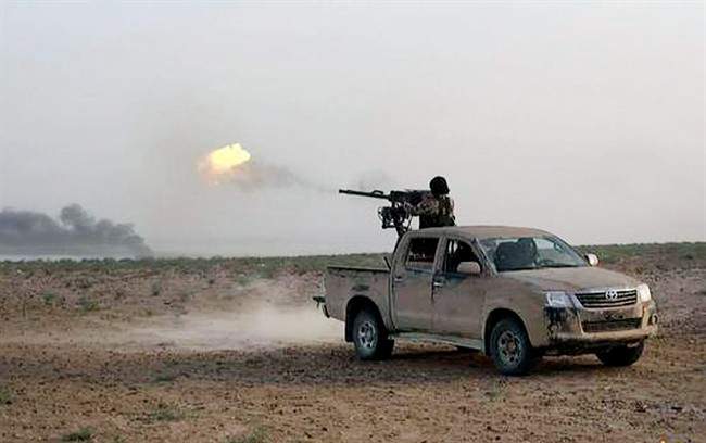 In this picture released on Wednesday, May 20, 2015 by the website of Islamic State militants, an Islamic State fighter fires his weapon during a battle against Syrian government forces on a road between Homs and Palmyra, Syria.