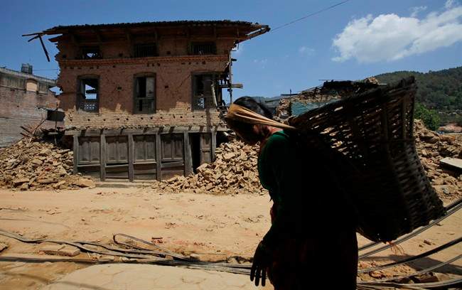 A Nepalese woman carries a basket and walks past a damaged house in Kathmandu, Nepal, Saturday, May 2, 2015.
