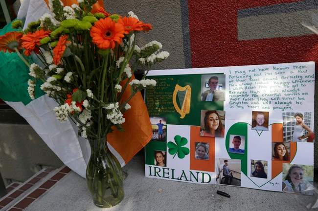 A flag of Ireland, flowers and a sign are shown at a shrine left for victims of the Library Gardens apartment building balcony collapse Wednesday, June 17, 2015. The balcony broke loose from the building during a 21st birthday party early Tuesday, killing several people and seriously injuring others.