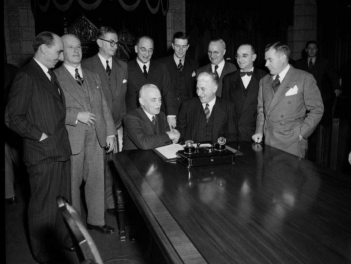 Ottawa, Ontario; December 11,1948–Confederation — Newfoundland and Canadian Government delegation signing the agreement admitting Newfoundland to Confederation. Prime Minister Louis S. St.Laurent and Hon. A. J. Walsh shake hands following signing of agreement.(