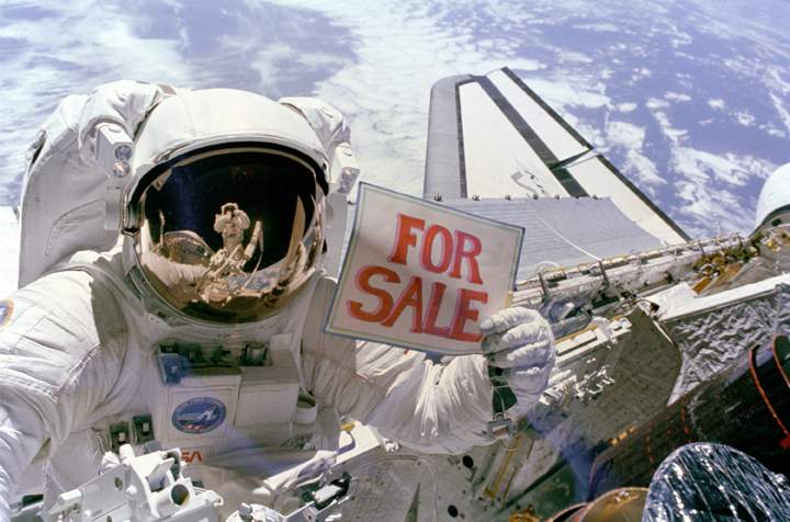 Astronaut Dale Gardner holds up a “For Sale” sign referring to two satellites that were retrieved during a spacewalk on Nov. 14, 1984.