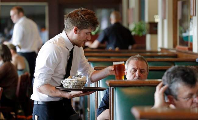 FILE - In this May 14, 2014, file photo, waiter Spencer Meline serves a customer at Ivar's Acres of Clams restaurant on the Seattle waterfront. Two new reports examining the impact of a minimum wage increase in the city delivered conflicting results.
