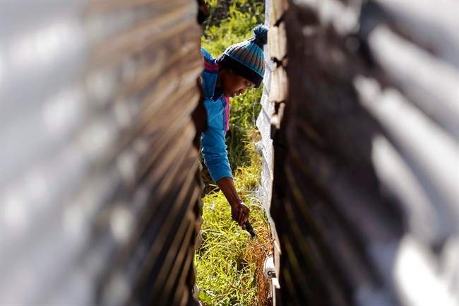 A child paints a shack with white fire retardant paint as a contribution to International Nelson Mandela day celebrating former South African president Mandela's birthday in the township of Nomzamo, South Africa, Saturday, July 18, 2015. 