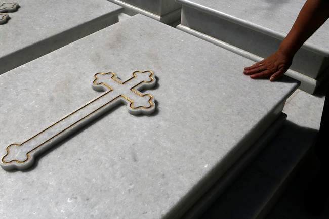 A woman touches a grave at a cemetery in Athens, Friday, July 17, 2015.