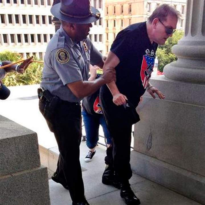 In this photo provided by Rob Godfrey, police officer Leroy Smith, left, helps a man wearing National Socialist Movement attire up the stairs during a rally Saturday, July 18, 2015, in Columbia, S.C. Members of the group were protesting Saturday the removal of the Confederate flag from the Statehouse grounds earlier this month. (Rob Godfrey via AP)