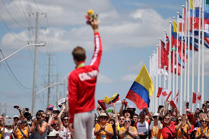 Cycling fans celebrate as Canada’s Hugo Houle stands on the podium wearing his gold medal after the men’s individual time trial cycling competition at the Pan Am Games in Milton, Ontario on Wednesday, July 22, 2015.