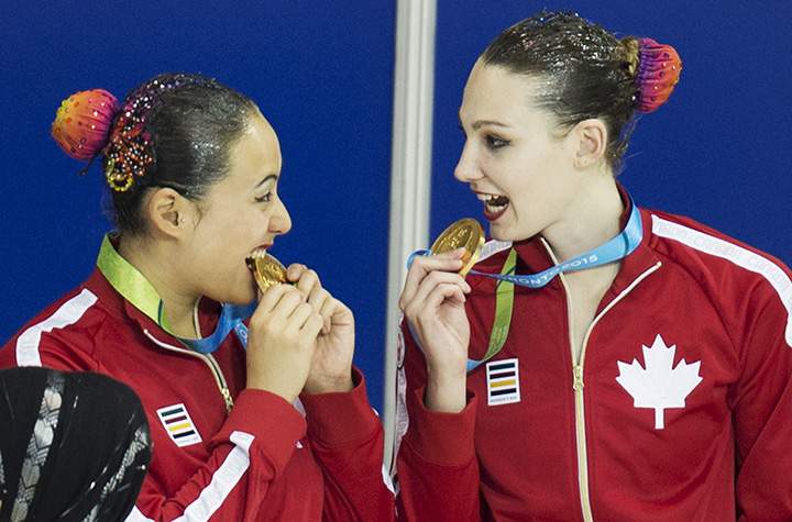 Canadian synchronized swimmers Marie-Lou Morin (L) and Samantha Nealon (R) bite their gold medals after finishing first in the Team Free Finals at the 2015 Pan American Games in Toronto on July 11, 2015.