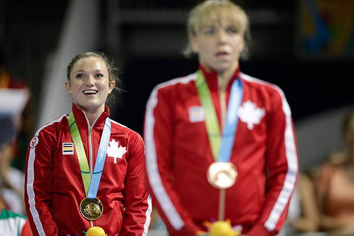 Canada’s Rosie MacLennan, left, and teammate Karen Cockburn listen to the national anthem after women’s trampoline competition in the Pan Am Games in Toronto Sunday, July 19, 2015.