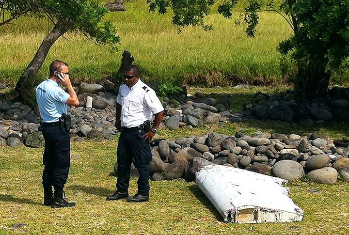 Policemen stand next to a piece of debris from an unidentified aircraft found in the coastal area of Saint-Andre de la Reunion on July 29, 2015.