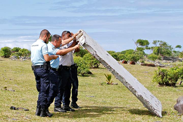 In this photo dated Wednesday, July 29, 2015, French police officers inspect a piece of debris from a plane in Saint-Andre, Reunion Island.
