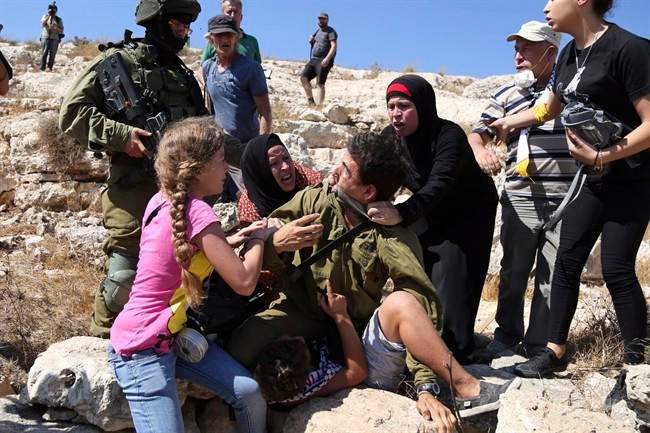 In this Friday, Aug, 28, 2015 photo, Palestinian women and youth scuffle with an Israeli soldier trying to arrest a 12-year-old boy during a protest near the West Bank village of Nebi Saleh.