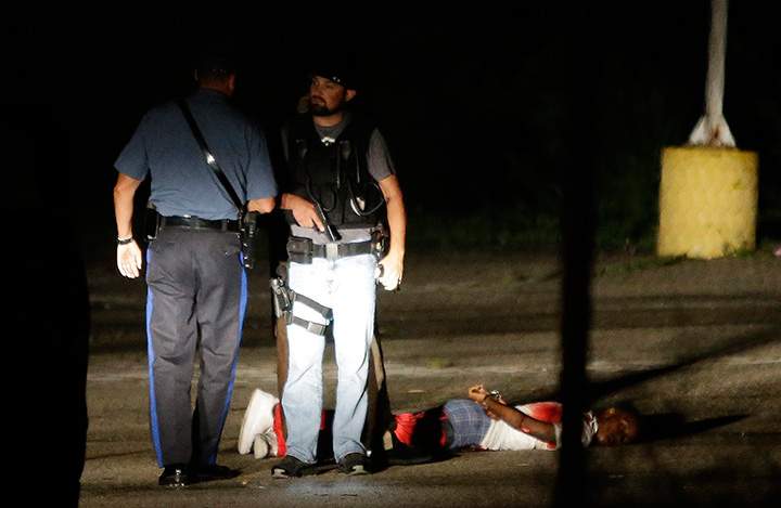 Police stand near a suspect in a parking lot after gunfire erupted during a protest on the anniversary of the death of Michael Brown, Sunday, Aug. 9, 2015, in Ferguson, Mo.