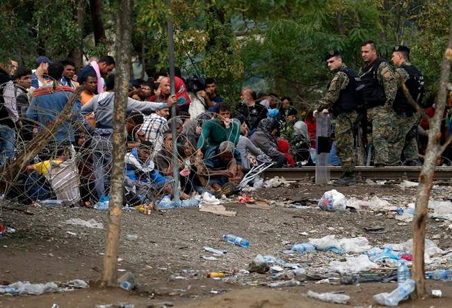 Migrants stand behind the barbed wire set by Macedonian police to stop thousands of migrants entering Macedonia illegally from Greece, near the southern Macedonian town of Gevgelija, Saturday, Aug. 22, 2015. About 39,000 people, mostly Syrian migrants, have been registered as passing through Macedonia in the past month, twice as many as the month before. (AP Photo/Darko Vojinovic).