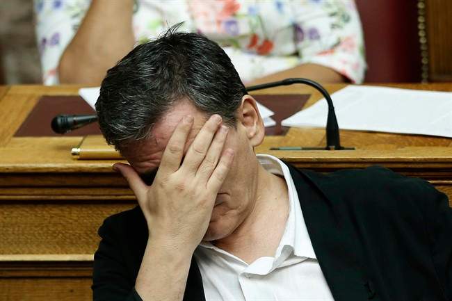 Greek Finance Minister Euclid Tsakalotos covers his face during a parliamentary session in Athens, early Friday, Aug. 14, 2015. The Greek government defended its new bailout program in tumultuous parliamentary sessions as it faced a rebellion in the governing Syriza party ahead of a vote on the deal. (AP Photo/Yannis Liakos).