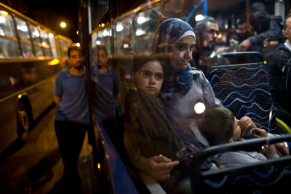 A woman and her children sit as they have boarded a bus provided by Hungarian authorities for migrants and refugees at Keleti train station in Budapest, Hungary, Saturday, Sept. 5, 2015. Hundreds of migrants boarded buses provided by Hungary’s government as Austria in the early-morning hours said it and Germany would let them in. Austrian Chancellor Werner Faymann announced the decision early Saturday after speaking with Angela Merkel, his German counterpart – not long after Hungary’s surprise nighttime move to provide buses for the weary travelers from Syria, Iraq and Afghanistan.