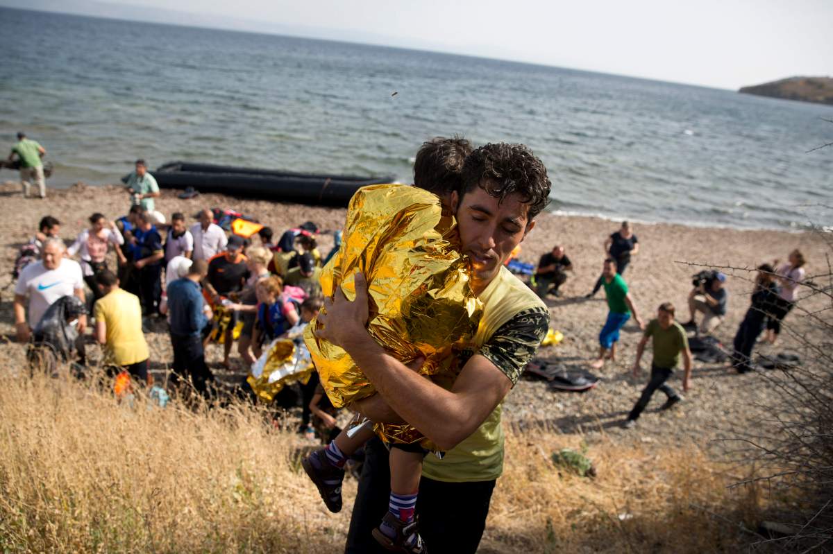 A Syrian man carries a child wrapped in a thermal blanket as they arrive with others at the coast on a dinghy after crossing from Turkey, at the island of Lesbos, Greece, Monday, Sept. 7, 2015.