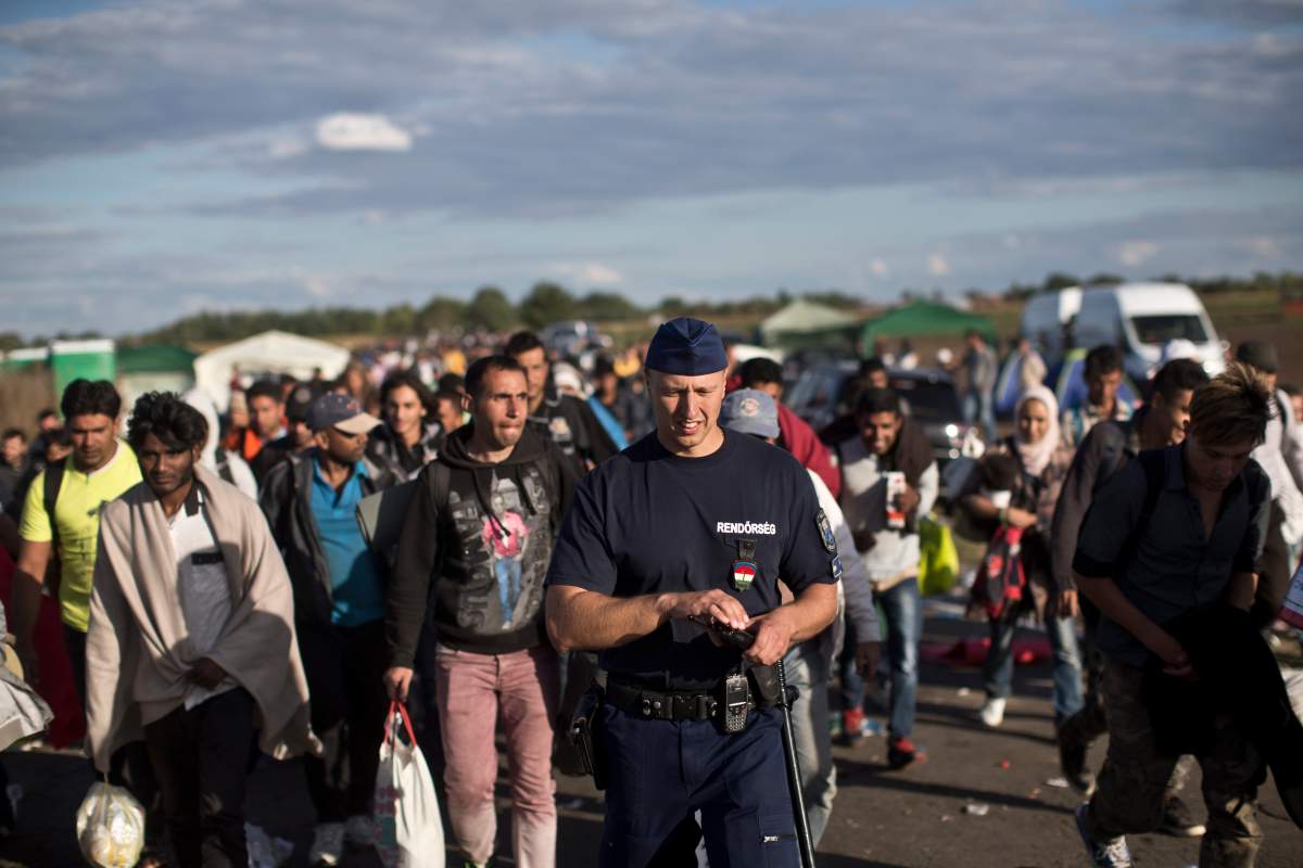 Hungarian police officer is overwhelmed by the numbers of migrants, as he walks with a group of people that walked out of a temporary holding center controlled by Hungarian authorities in Roszke, southern Hungary, Monday, Sept. 7, 2015, inside Hungary, just over the border from Serbia. The situation is confused with many hundreds of migrants moving in several directions and trying to reach a migrant registration camp, rather than wait for a unreliable bus service.(AP Photo/Marko Drobnjakovic)