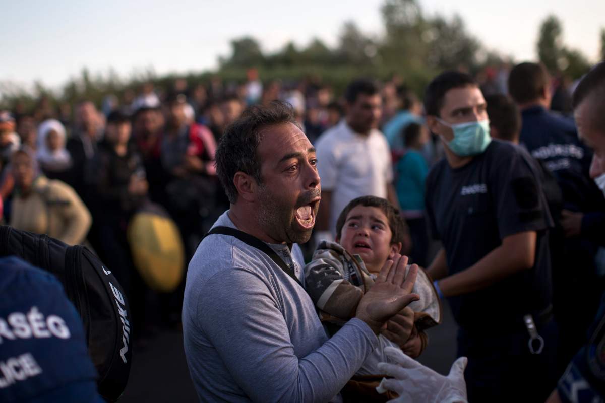 A man holds his child as he tries to talk to Hungarian police officers in Roszke, Hungary, Monday, Sept. 7, 2015, as the migrants move away from a temporary holding center controlled by Hungarian authorities, just over the border from Serbia.  The situation is confused with many hundreds of migrants moving in several directions and trying to reach a migrant registration camp, rather than wait for a unreliable bus service.