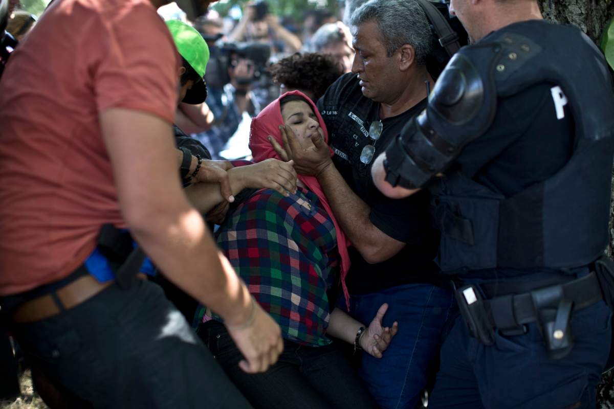 A woman faints after she pushed through a police line in Tovarnik, Croatia, Thursday, Sept. 17, 2015. Hundreds of migrants have pushed through police lines in the eastern Croatian town of Tovarnik, with people trampling and falling on each other amid the chaos, as more than 2,000 men, women and children were stuck at the local train station for hours in blazing heat and sun on Thursday, waiting to board trains and buses for transport to refugee centers.