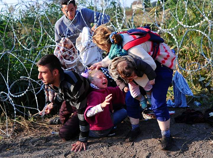 A young migrant’s hair becomes stuck while crawling under a barbed fence with her family at the Hungarian-Serbian border near Roszke, on August 27, 2015.